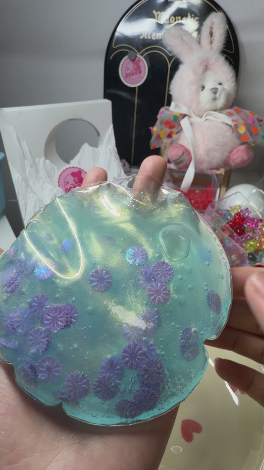 Shimmery mermaid‑blue transparent squishy pouch decorated with holographic purple daisies. Ultra‑soft texture, flows smoothly with only a light squeeze, calming aesthetic viral stress relief fidget toy.