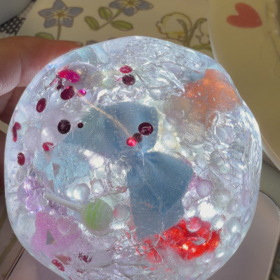 6cm handmade crystal clear squishy toy filled with blue bow, beads and sequins. Soft light‑force texture, keeps shape after squeezing with addictive finger‑suction rebound, satisfying ASMR stress relief fidget toy.
