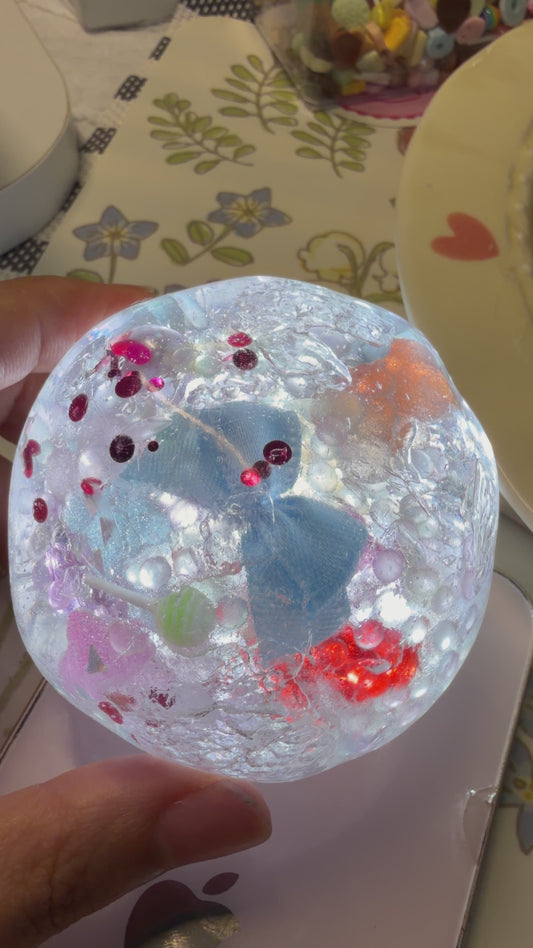 6cm handmade crystal clear squishy toy filled with blue bow, beads and sequins. Soft light‑force texture, keeps shape after squeezing with addictive finger‑suction rebound, satisfying ASMR stress relief fidget toy.
